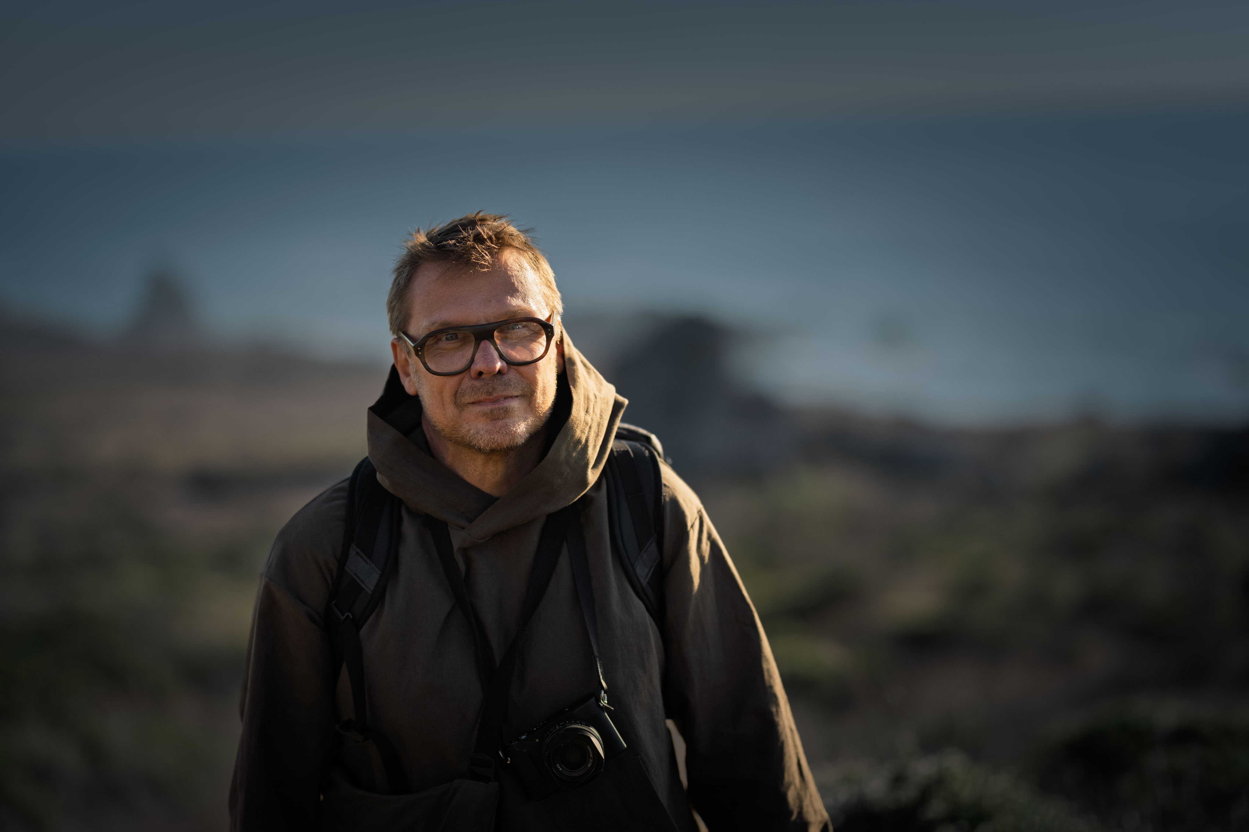 Timo Arnall on a hillside at dusk, with a camera around his neck
